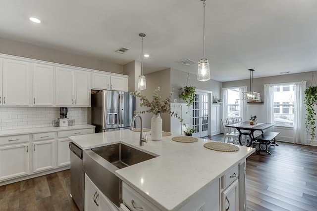 kitchen featuring an island with sink, sink, white cabinets, hanging light fixtures, and stainless steel appliances