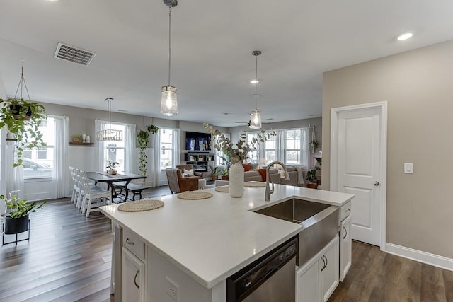 kitchen featuring dark wood-type flooring, dishwasher, white cabinetry, hanging light fixtures, and an island with sink