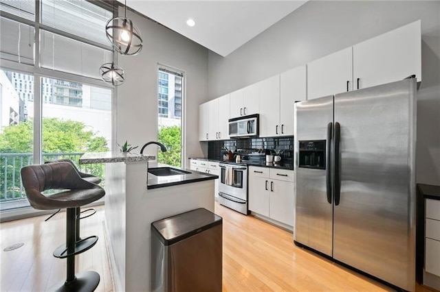 44 Peachtree Pl NW Unit 528, Atlanta, GA 30309 - kitchen with stainless steel appliances, a sink, light wood-type flooring, white cabinetry, and decorative backsplash
