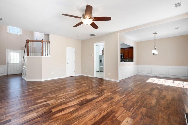 unfurnished living room with a ceiling fan, visible vents, a decorative wall, and dark wood-style flooring