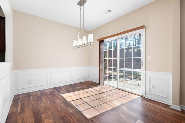 unfurnished dining area with visible vents, dark wood-style flooring, a notable chandelier, and wainscoting