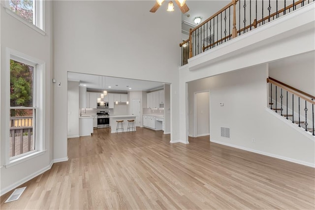 unfurnished living room with visible vents, light wood-type flooring, stairs, and baseboards