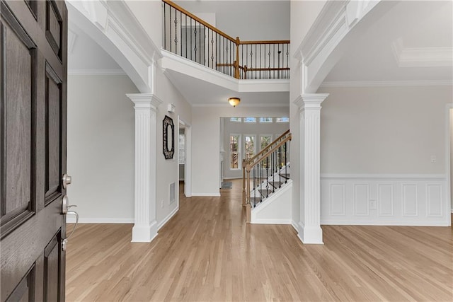 foyer with crown molding, light wood-style flooring, decorative columns, and arched walkways