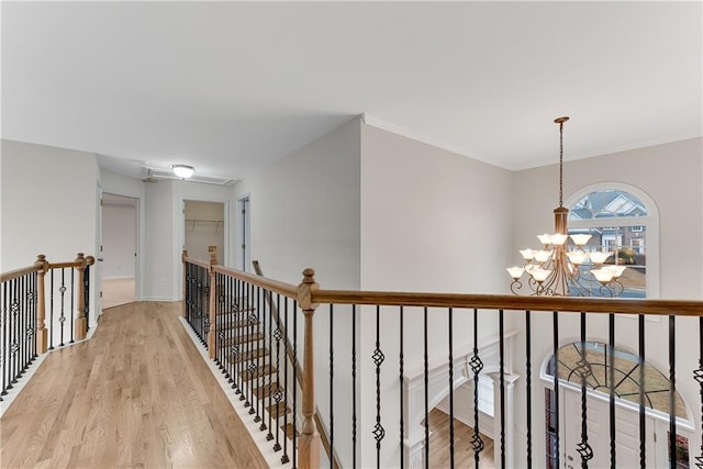 hallway with an upstairs landing, a notable chandelier, light wood-style flooring, and ornamental molding