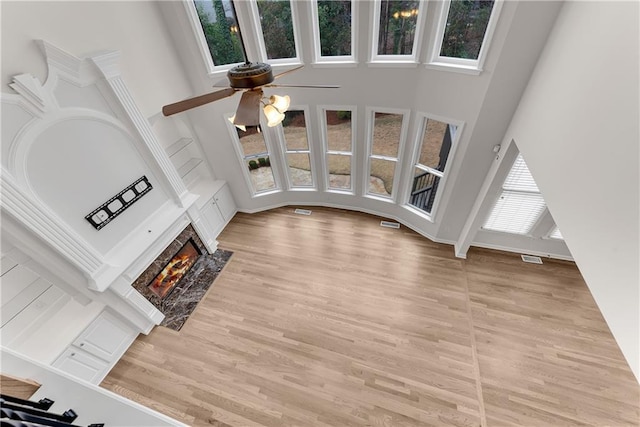 unfurnished living room featuring a fireplace with flush hearth, light wood-style flooring, and a towering ceiling