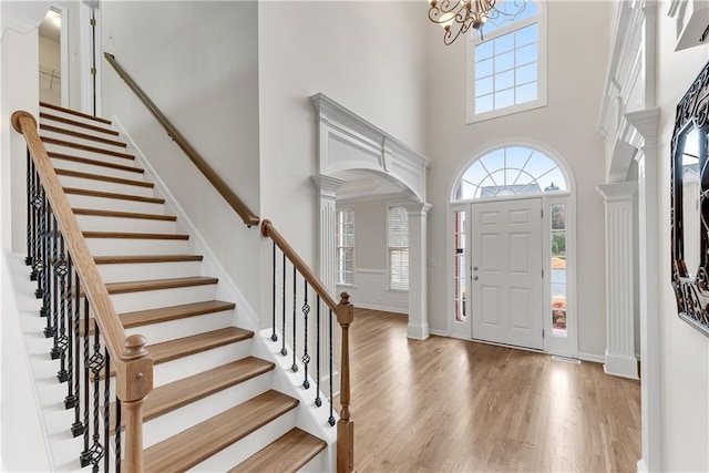 entryway featuring a notable chandelier, a high ceiling, wood finished floors, and ornate columns