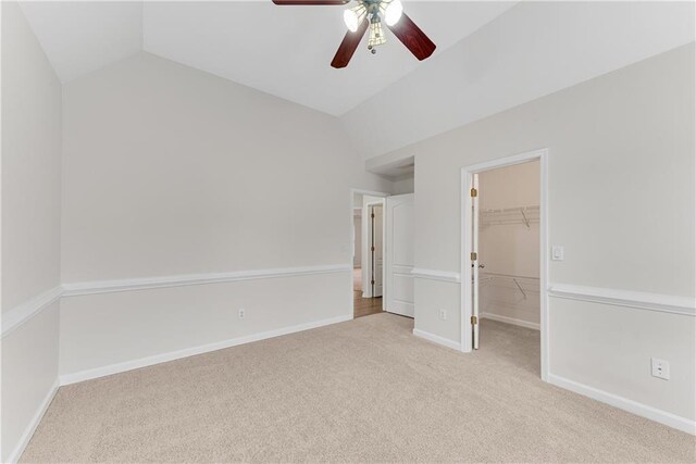 unfurnished bedroom with baseboards, vaulted ceiling, a closet, light carpet, and a walk in closet