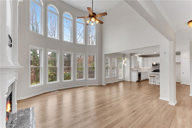 unfurnished living room with light wood-type flooring, a sink, a premium fireplace, baseboards, and ceiling fan