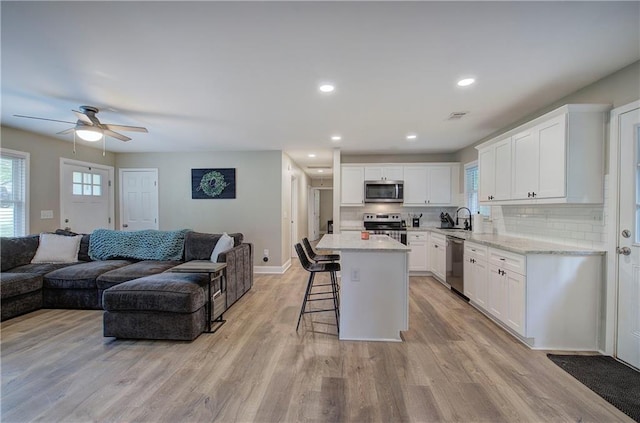 kitchen with a sink, a breakfast bar, open floor plan, a ceiling fan, and appliances with stainless steel finishes