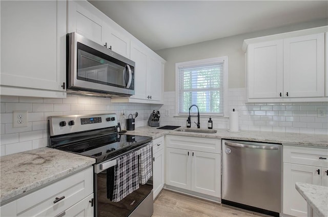 kitchen featuring tasteful backsplash, a sink, white cabinets, stainless steel appliances, and light wood-style flooring