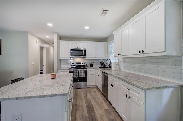 kitchen featuring visible vents, wood finished floors, a kitchen island, a sink, and stainless steel appliances