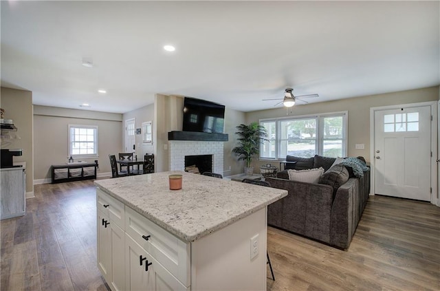 kitchen with white cabinets, a brick fireplace, light wood-style flooring, a center island, and a ceiling fan