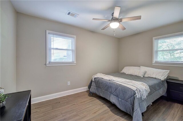 bedroom featuring baseboards, a ceiling fan, wood finished floors, and visible vents