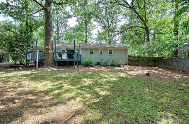 rear view of house with a lawn, brick siding, fence, and a wooden deck