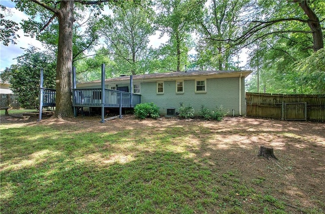 rear view of property featuring fence, a deck, brick siding, central AC unit, and a yard