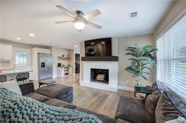 living room with light wood finished floors, a brick fireplace, a ceiling fan, baseboards, and visible vents