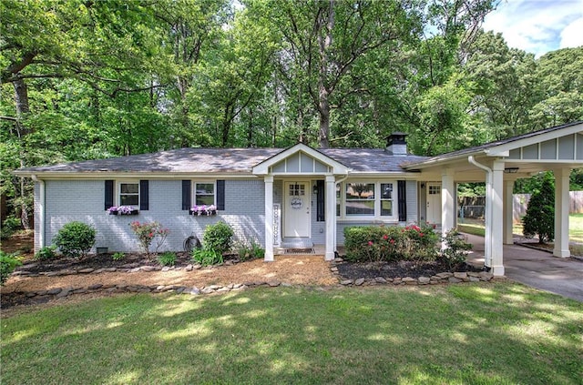 ranch-style home featuring a chimney, brick siding, a front yard, and a carport