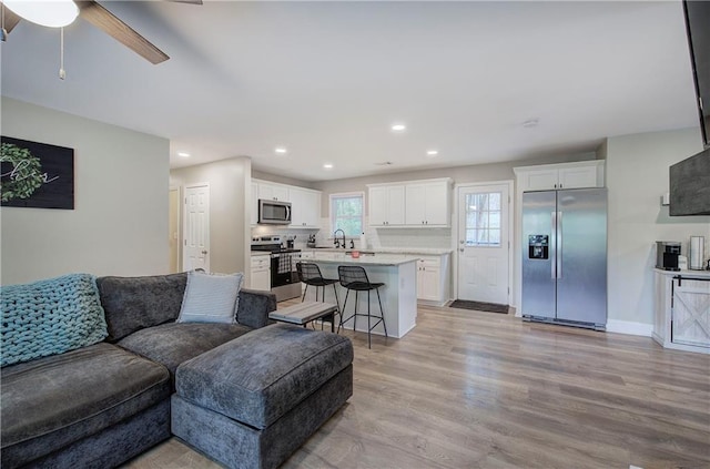living room featuring recessed lighting, a ceiling fan, baseboards, and light wood-type flooring