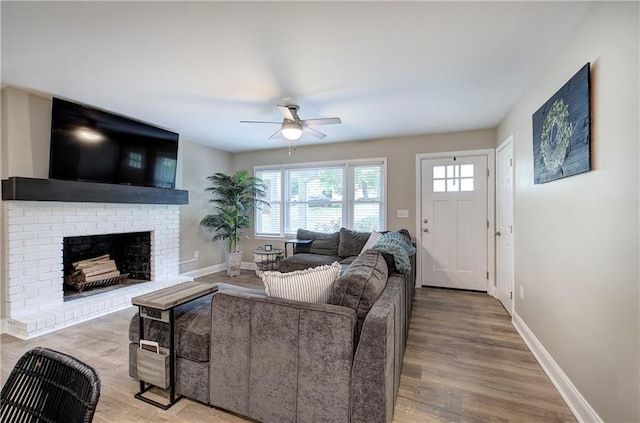 living room with baseboards, a ceiling fan, a brick fireplace, and wood finished floors
