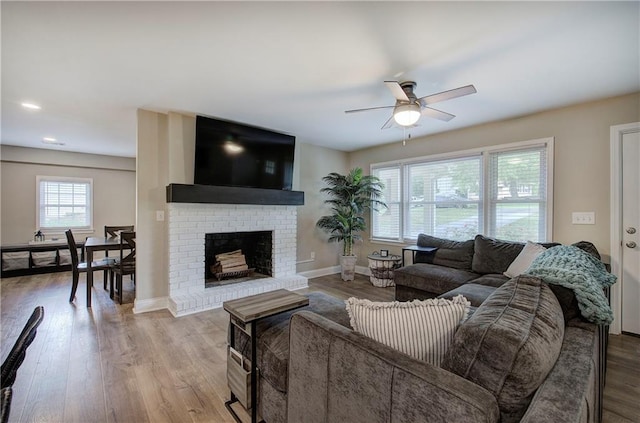 living room featuring baseboards, ceiling fan, a brick fireplace, and wood finished floors