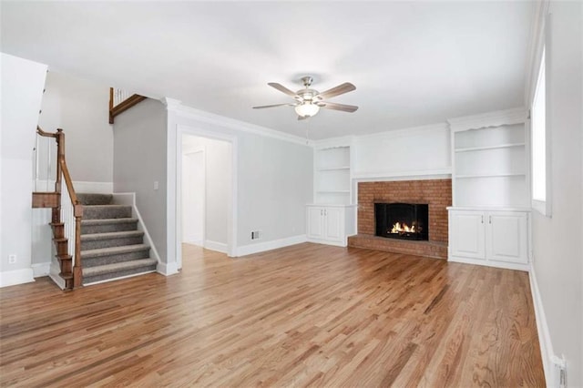 unfurnished living room with a brick fireplace, ceiling fan, built in shelves, ornamental molding, and light hardwood / wood-style floors