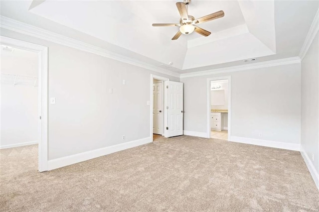 unfurnished bedroom with ceiling fan, light colored carpet, a tray ceiling, a walk in closet, and ornamental molding