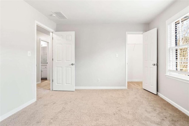 unfurnished bedroom with multiple windows, a walk in closet, a closet, and light colored carpet