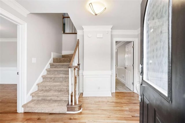 entryway with ornamental molding and light hardwood / wood-style flooring