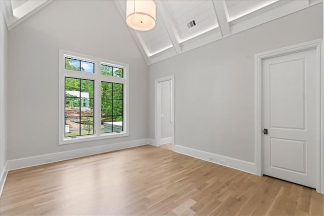 unfurnished room with high vaulted ceiling, beamed ceiling, and light wood-type flooring