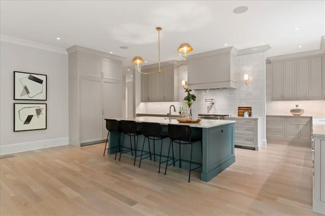 kitchen featuring a breakfast bar area, a kitchen island with sink, backsplash, decorative light fixtures, and light wood-type flooring