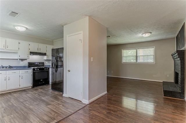 2783 Bicentennial Dr, Stone Mountain, GA 30087 - kitchen featuring black appliances, under cabinet range hood, a textured ceiling, dark wood finished floors, and a fireplace