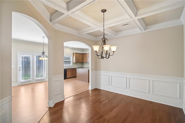 unfurnished dining area featuring a notable chandelier, coffered ceiling, wood finished floors, visible vents, and beam ceiling