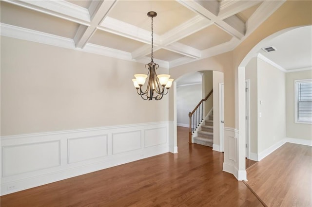 unfurnished dining area featuring arched walkways, beamed ceiling, stairway, and wood finished floors