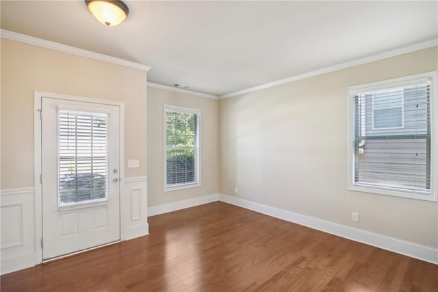 doorway to outside with a wealth of natural light, a wainscoted wall, crown molding, and wood finished floors