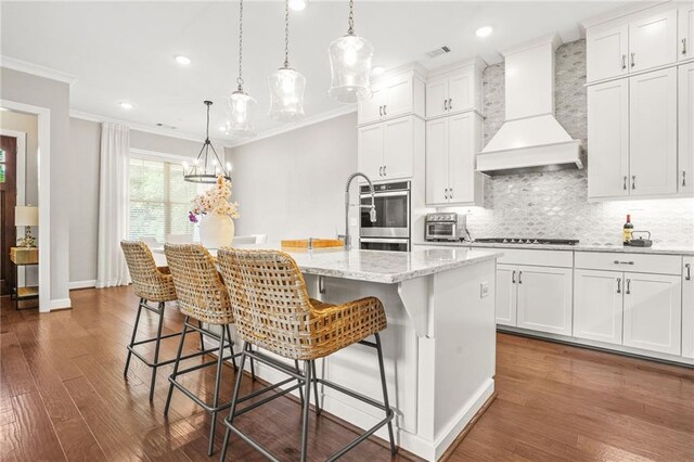 kitchen with ornamental molding, decorative backsplash, custom exhaust hood, a center island with sink, and gas stovetop