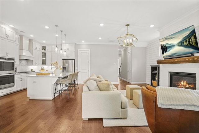 living area with dark wood-style flooring, an inviting chandelier, a fireplace, recessed lighting, and ornamental molding
