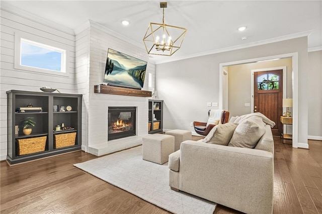 living area featuring crown molding, an inviting chandelier, a brick fireplace, recessed lighting, and wood finished floors