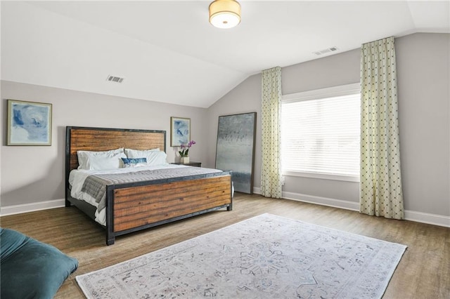 bedroom with visible vents, baseboards, wood finished floors, and vaulted ceiling