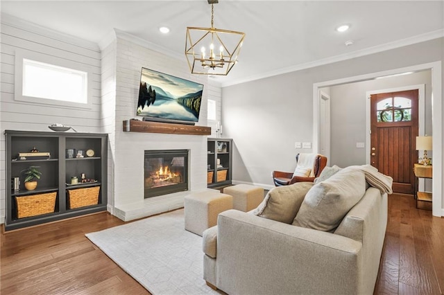 living area featuring a large fireplace, wood finished floors, a notable chandelier, ornamental molding, and recessed lighting
