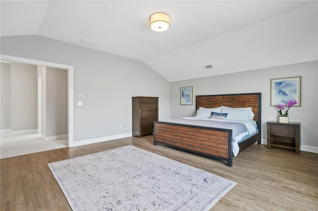 bedroom with baseboards, visible vents, wood finished floors, and lofted ceiling