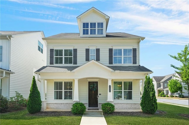 traditional style home with covered porch, a front yard, and roof with shingles