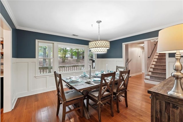 dining room with a wainscoted wall, crown molding, and wood-type flooring