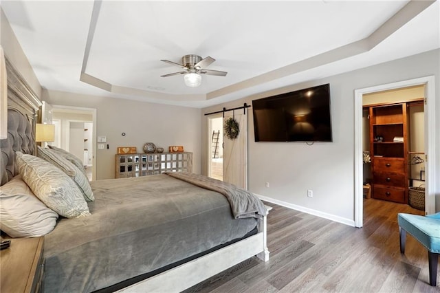 bedroom featuring a tray ceiling, baseboards, a barn door, ceiling fan, and wood finished floors