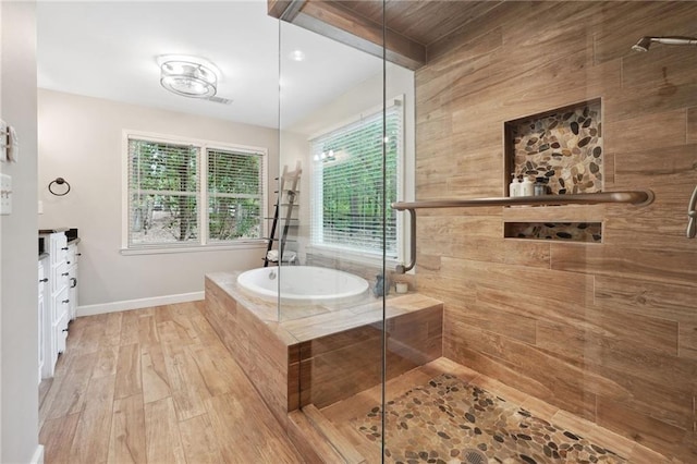bathroom featuring vanity, a bath, baseboards, a shower stall, and wood finished floors