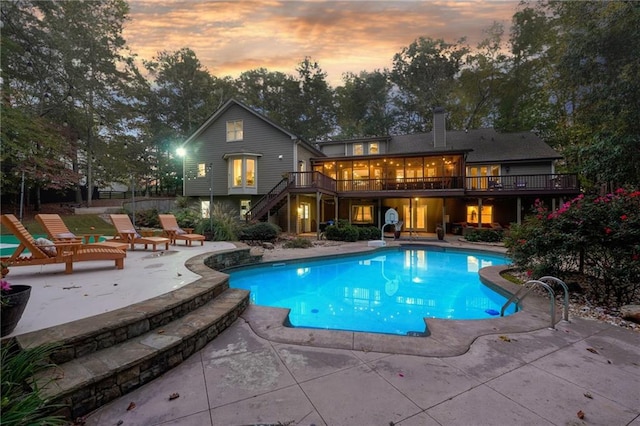pool at dusk featuring stairs, an outdoor pool, a wooden deck, and a patio area