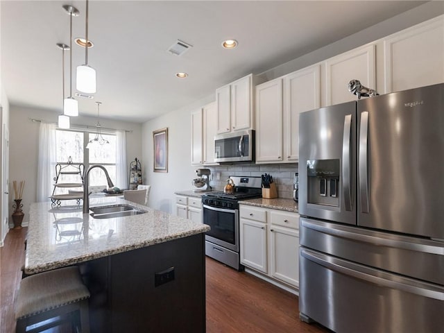 kitchen featuring tasteful backsplash, visible vents, light stone countertops, stainless steel appliances, and a sink