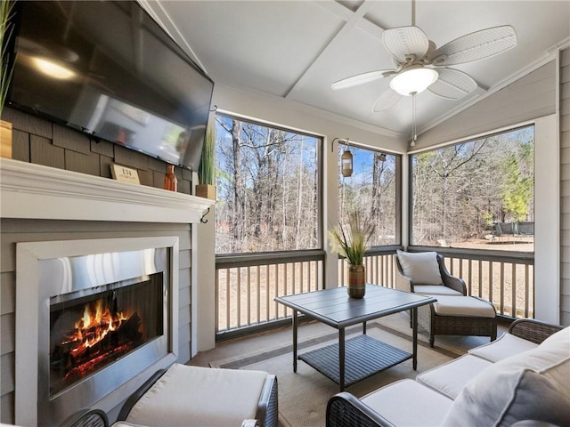 sunroom featuring a warm lit fireplace, ceiling fan, and vaulted ceiling