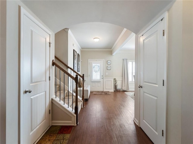 entrance foyer featuring dark wood finished floors, stairway, arched walkways, crown molding, and a decorative wall