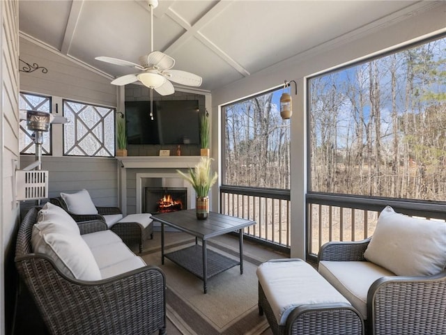 sunroom featuring beamed ceiling, a large fireplace, and ceiling fan