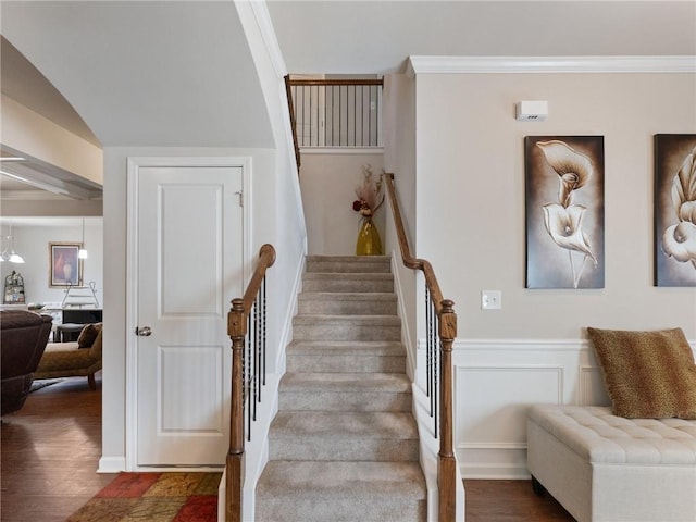 stairway with a wainscoted wall, crown molding, and wood finished floors